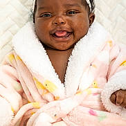 Rhea is registered to the contest to win money with this photo: baby, infant, child, smiling, tongue_out, portrait, close_up, headband, flower, pink, robe, blanket, fluffy, cozy, lying_down, indoor, face, hair, happy, photography