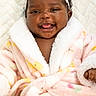 baby, infant, child, smiling, tongue_out, portrait, close_up, headband, flower, pink, robe, blanket, fluffy, cozy, lying_down, indoor, face, hair, happy, photography