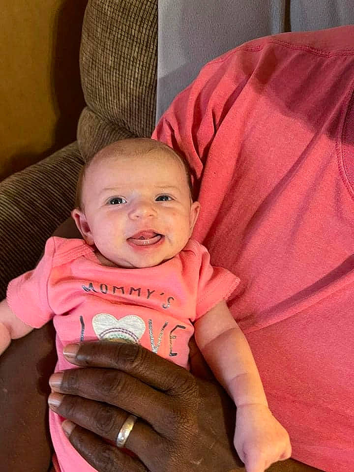 Micaela is registered to the contest to win money with this photo: baby, baby_carriage, baby_products, baby_toddler_clothing, cheek, child, comfort, gesture, hand, happy, head, human_body, iris, lap, person, pink, sleeve, smile, textile, thumb