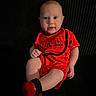 baby, child, red_clothing, sitting, couch, indoor, portrait, infant, cute, happy, face, legs, hand, sock, shorts, tshirt, background, expression, person, photography