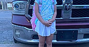 Sophia joined the competition — help win amazing prizes! child, girl, smiling, outdoor, pickup_truck, vehicle, backpack, sneakers, shorts, shirt, standing, portrait, frontyard, driveway, residential, blue_sky, daylight, grille, ram_truck, playful