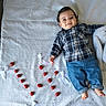 Adam participe au concours pour gagner de l'argent avec cette photo : baby, child, plaid_shirt, jeans, barefoot, smiling, lying_down, red_tomatoes, white_bows, heart_shape, star_pattern, sheet, plush_toy, indoors, cute, happy, portrait, infant, casual_clothing, decorative_arrangement