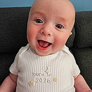 Theo joined the competition — help win amazing prizes! baby, smiling, happy, infant, onesie, clothing, face, head, skin, person, cute, indoors, couch, furniture, blue_background, ribbed_texture, open_mouth, cheerful, child, portrait