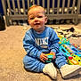 baby, blue_sweatshirt, carpet, child, childhood, clothing, crib, cute, floor, home, indoor, nike, person, playful, room, sitting, smiling, toddler, toy, white_sneakers