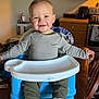 Wyatt is registered to the contest to win money with this photo: toddler, child, smiling, booster_seat, table, kitchen, wooden_cabinet, oven, sneakers, clothing, long_sleeve_shirt, pants, face, person, indoor, happy, furniture, high_chair, home, casual