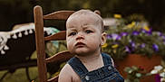 Wyatt joined the competition — help win amazing prizes! baby, background_blur, casual_clothing, child, closeup, cute, daylight, denim_overalls, flowers, garden, greenery, infant, nature, outdoor, person, plant, portrait, serious_expression, summer, wooden_chair