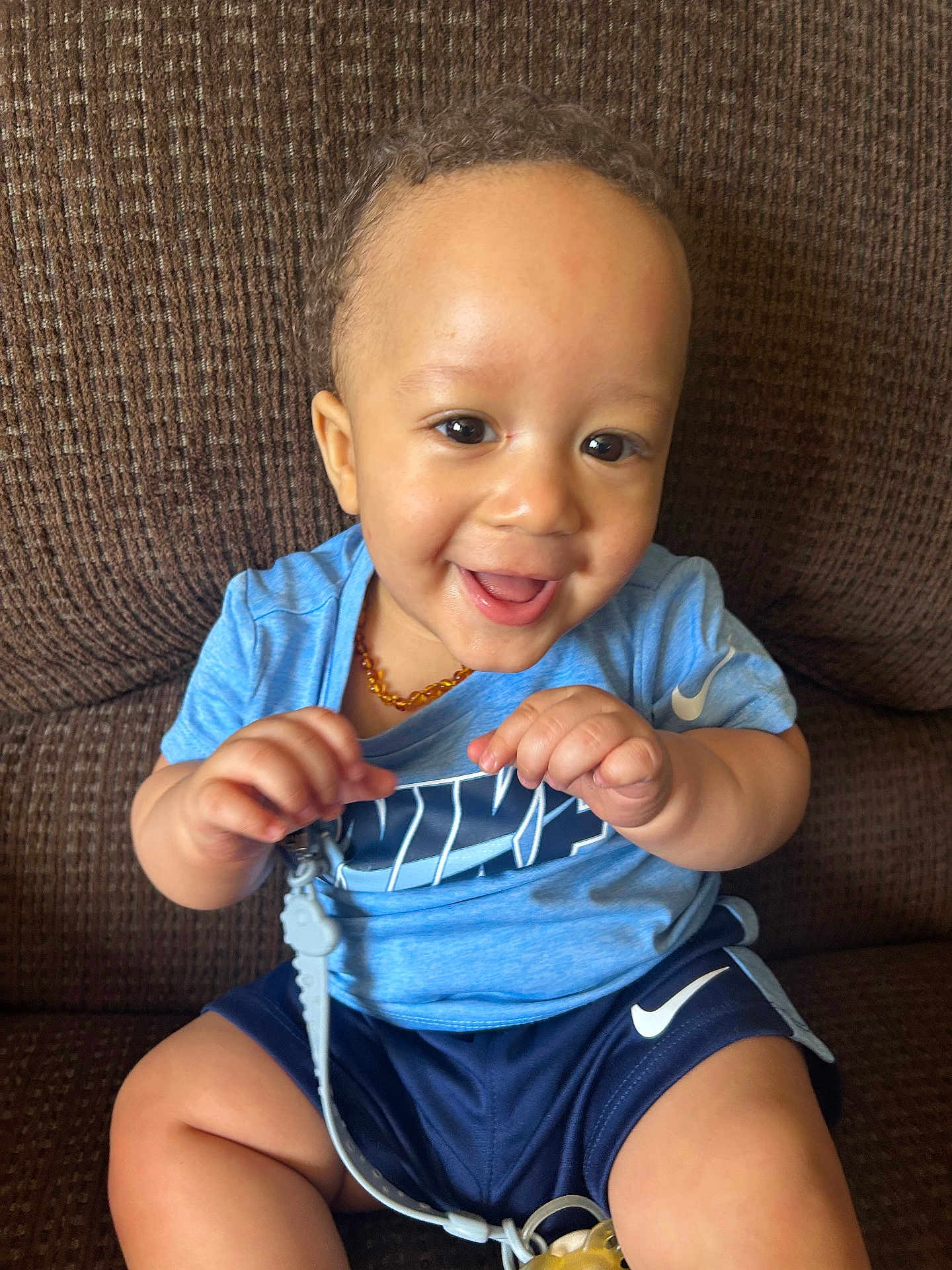 Ajion is registered to the contest to win money with this photo: toddler, child, smiling, happy, curly_hair, blue_shirt, nike, shorts, sitting, couch, indoor, toy, clip_on, playful, cute, baby, portrait, person, hand, face