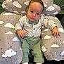 baby, infant, child, cushion, cloud_pattern, green_pants, striped_shirt, bow_tie, socks, indoor, portrait, cute, relaxing, seated, fabric, soft_toy, small_hands, big_eyes, comfortable, casual_clothing