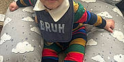 Ajion joined the competition — help win amazing prizes! baby, child, infant, bib, colorful_clothing, striped_outfit, white_shoes, cushion, cloud_pattern, carpet, indoor, cute, smiling, face, sitting, footwear, sock, person, young_child, curious