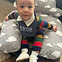 baby, child, infant, bib, colorful_clothing, striped_outfit, white_shoes, cushion, cloud_pattern, carpet, indoor, cute, smiling, face, sitting, footwear, sock, person, young_child, curious