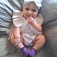 Kinsey is registered to the contest to win money with this photo: baby, child, infant, smiling, happy, sitting, portrait, bow, headband, dress, floral_pattern, purple_socks, finger_in_mouth, bed, bedding, indoors, gray_background, candid, adorable, photography