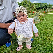 Siyana participe au concours pour gagner de l'argent avec cette photo : baby, child, flower, grass, garden, bib, headwrap, adult, person, outdoor, nature, greenery, cloudy_sky, footwear, cute, smiling, park, casual_clothing, standing, holding