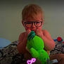 toddler, child, plush_toy, bed, blanket, indoor, glasses_overlay, hearts_overlay, sitting, cute, toy, baby, soft_toy, person, young_child, fun, digital_effects, comfort, cozy, playful