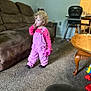 toddler, child, pink_overalls, curly_hair, living_room, carpet, couch, table, sippy_cup, high_chair, toy, person, indoor, furniture, thinking, clothing, floor, footwear, wall, door
