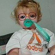 Aubrianna is registered to the contest to win money with this photo: toddler, child, indoor, pacifier, glasses_filter, curly_hair, white_shirt, logo, hand, seated, furniture, face, person, expression, casual, closeup, young_child, cute, funny, wearing