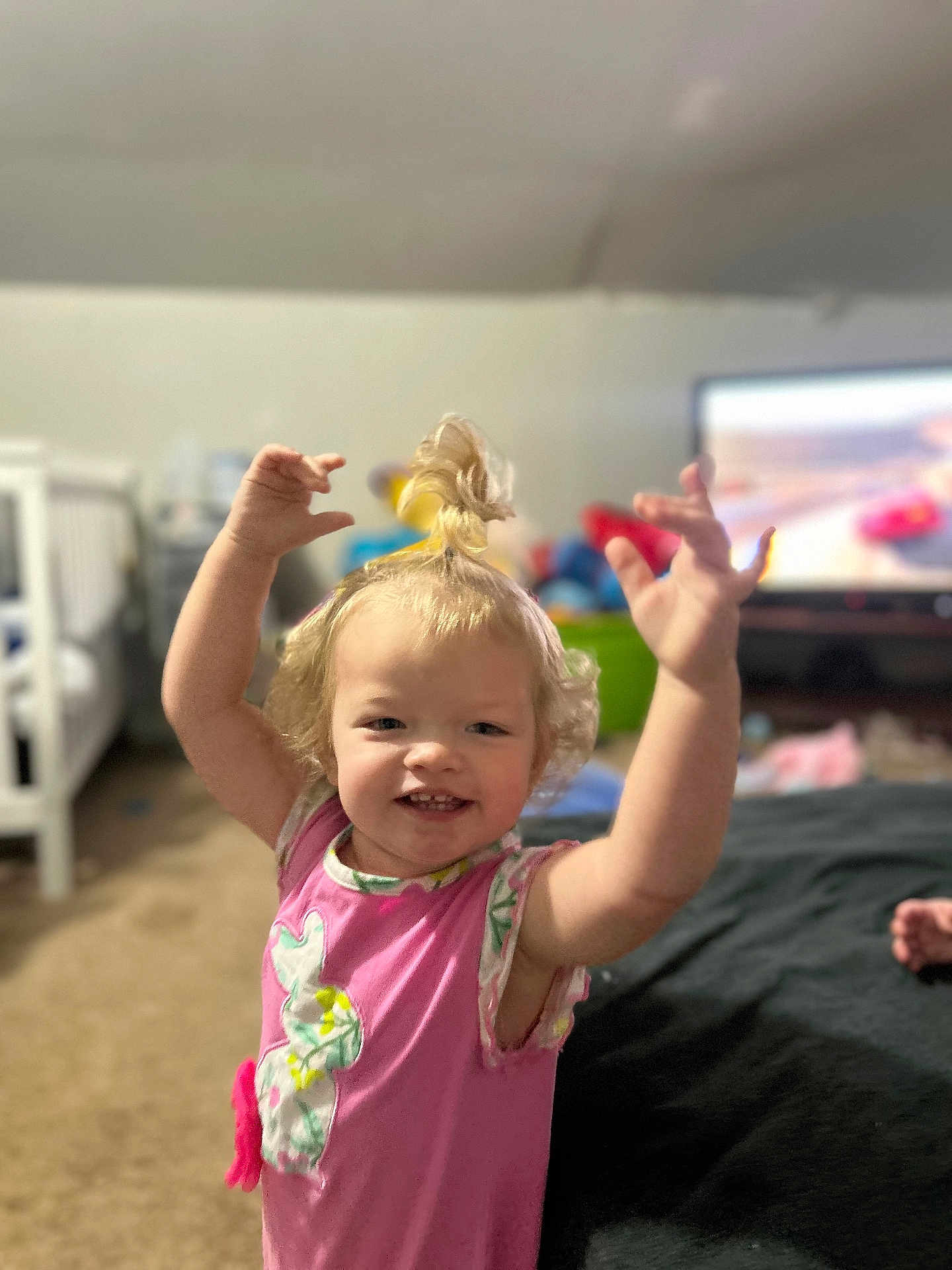 Aubrianna joined the competition — help win amazing prizes! toddler, child, smile, happy, pink_clothing, blonde_hair, indoor, carpet, crib, television, cartoon, toy, person, raising_arms, curly_hair, playful, living_room, cute, expression, home