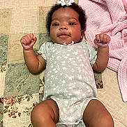 Amara is registered to the contest to win money with this photo: baby, infant, child, portrait, lying_down, smiling, fists, hair_bow, flower, onesie, floral_pattern, pink_blanket, patchwork_quilt, bed, bedding, indoor, cozy, adorable, photography, safe
