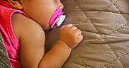 Amara joined the competition — help win amazing prizes! baby, infant, child, face, pacifier, pink_clothing, curly_hair, lying_down, bed, quilt, blanket, hand, arm, portrait, side_profile, indoors, cozy, sleeping_area, close_up, candid