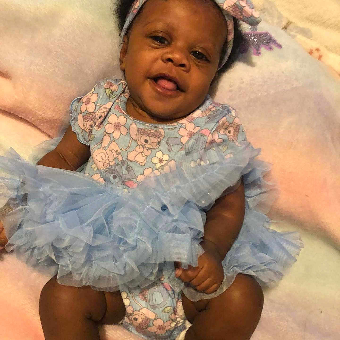 Kizzy Williams is registered to the contest to win money with this photo: baby, blanket, blue, child, clothing, cute, dress, face, footwear, happy, headband, indoors, infant, pastel, person, portrait, sitting, smile, soft, tutu