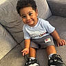 bright, casual_clothing, child, comfortable, couch, curly_hair, cute, footwear, happy, indoor, living_room, person, portrait, shorts, sitting, smile, sneakers, toddler, tshirt, young_child