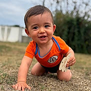 Arthur a rejoint le concours — aidez-le/la à gagner de superbes lots ! toddler, child, crawling, outdoor, grass, orange_clothing, smiling, happy, face, hand, wooden_sign, short_hair, nature, blurred_background, young_child, baby, playful, person, daylight, casual_wear