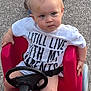Hunter joined the competition — help win amazing prizes! toddler, child, toy_car, steering_wheel, white_shirt, text_on_shirt, adult_legs, crocs, shorts, pavement, outdoor, cute, serious_expression, blonde_hair, blue_eyes, sitting, push_toy, funny_text, parent, summer_clothing