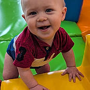 Hunter is registered to the contest to win money with this photo: baby, child, smiling, indoor, play_area, colorful, soft_play, padded, climbing, red_shirt, number_patch, happy, cute, toddler, hands, face, eyes, playground, fun, vibrant_colors
