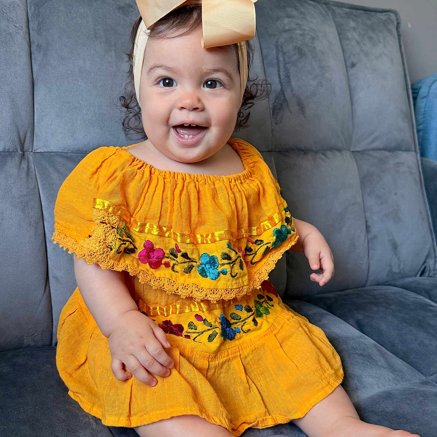 Jimena is registered to the contest to win money with this photo: baby, child, girl, smile, yellow_dress, bow, headband, sitting, couch, indoor, happy, cute, portrait, plush, furniture, embroidery, barefoot, person, young, bright