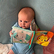 Freya joined the competition — help win amazing prizes! baby, infant, child, blue_onesie, soft_book, elephant, lion, striped_blanket, socks, cute, indoors, playing, seated, colorful_toys, fabric, pattern, happy, young_child, cozy, curious