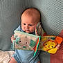 baby, infant, child, blue_onesie, soft_book, elephant, lion, striped_blanket, socks, cute, indoors, playing, seated, colorful_toys, fabric, pattern, happy, young_child, cozy, curious