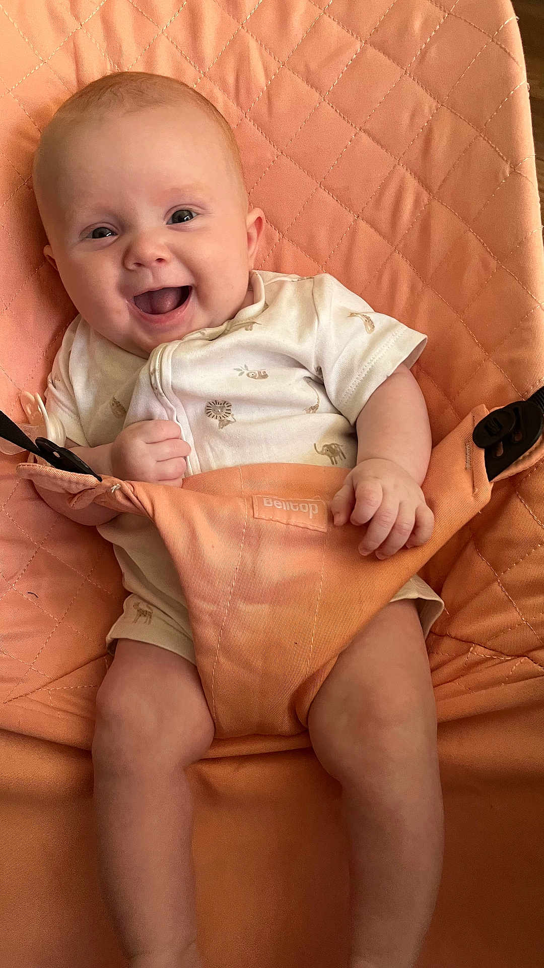 Freya is registered to the contest to win money with this photo: baby, smiling, infant, onesie, animal_print, seat, peach_color, happy, cute, child, skin, hand, legs, indoor, comfort, fabric, clothing, young, portrait, person