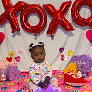 Yuri is registered to the contest to win money with this photo: baby, child, valentines_day, balloons, xoxo, heart, plush_toys, colorful, pajamas, cute, decorations, celebration, indoor, portrait, sitting, young_child, holiday, pink, purple, love