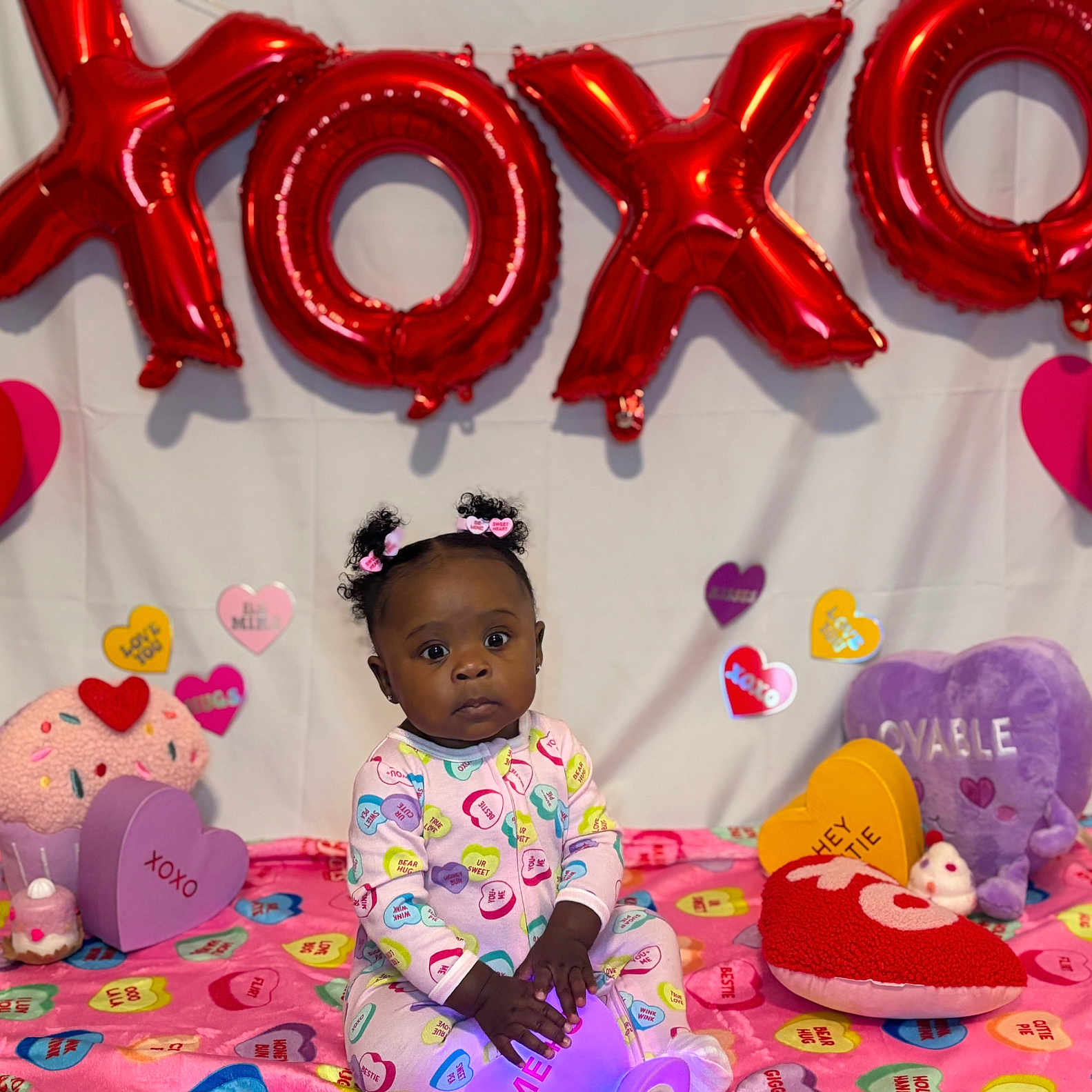 Yuri is registered to the contest to win money with this photo: baby, child, valentines_day, balloons, xoxo, heart, plush_toys, colorful, pajamas, cute, decorations, celebration, indoor, portrait, sitting, young_child, holiday, pink, purple, love