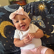 Violet is registered to the contest to win money with this photo: baby, child, smiling, pink_headband, bow, white_shirt, pink_shorts, blanket, moon, stars, butterfly, indoor, happy, sitting, cute, portrait, face, skin, hand, infant