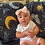 baby, infant, child, pink_headband, bow, white_shirt, pink_shorts, couch, blanket, celestial_pattern, moon, stars, butterfly, face, hands, indoor, home, decor, portrait, curious