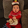 baby, child, red_clothing, christmas_hat, toy, knitted_toy, couch, cushion, white_socks, festive, indoor, cute, surprised_expression, seated, holiday, soft_lighting, infant, headwear, cozy, playful