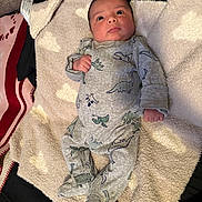 Isaai joined the competition — help win amazing prizes! baby, infant, child, portrait, lying_down, blanket, towel, onesie, dinosaur, dinosaur_print, gray_clothing, cozy, bed, bedding, indoor, wide_eyes, fist, sleepwear, textile, close_up