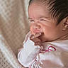 newborn, baby, infant, portrait, face, finger, hand, pink_clothing, blanket, cozy, indoors, close_up, dark_hair, sleepy, squinting, cute, gentle, soft_lighting, infant_hand, nursery