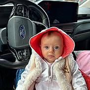 Charlotte participe au concours pour gagner de l'argent avec cette photo : baby, infant, hoodie, fur_vest, car_interior, steering_wheel, ford_logo, rain, window, seat, clothing, person, portrait, child, cute, sitting, looking_at_camera, indoors, weather, vehicle