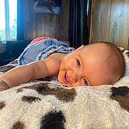 Penelope Grace is registered to the contest to win money with this photo: baby, smiling, blanket, indoor, wood_paneling, window, painting, arm, reaching, face, head, child, cozy, soft_texture, furniture, curtain, natural_light, happy, portrait, toddler