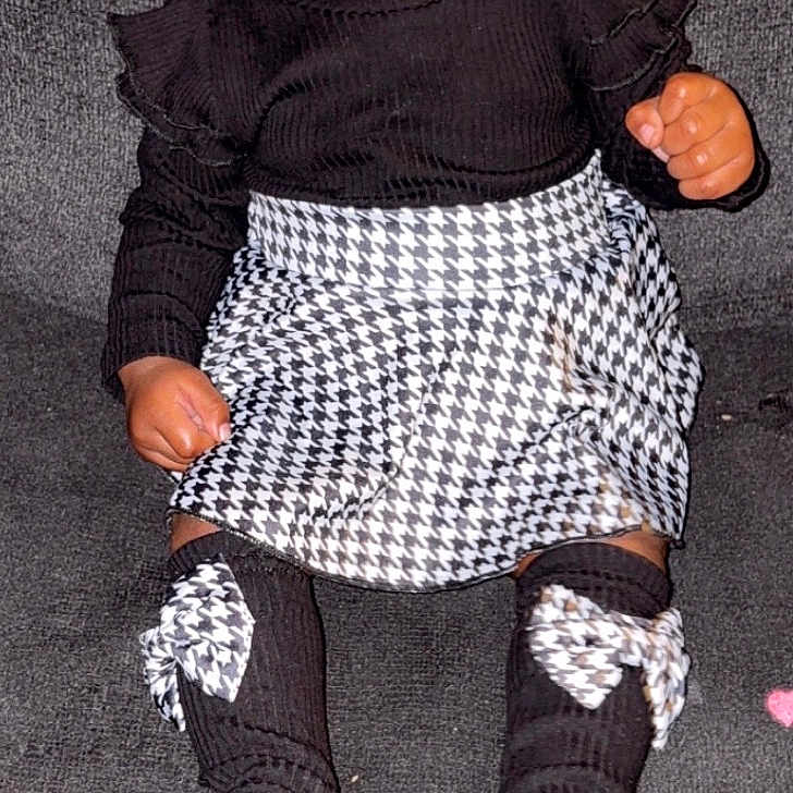 Audree joined the competition — help win amazing prizes! baby, black_clothing, bows, button_details, child, curious_expression, cute, dark_background, face, fashion, heart_shapes, houndstooth_pattern, indoor, patterned_skirt, person, portrait, sitting, socks, toddler, young_child