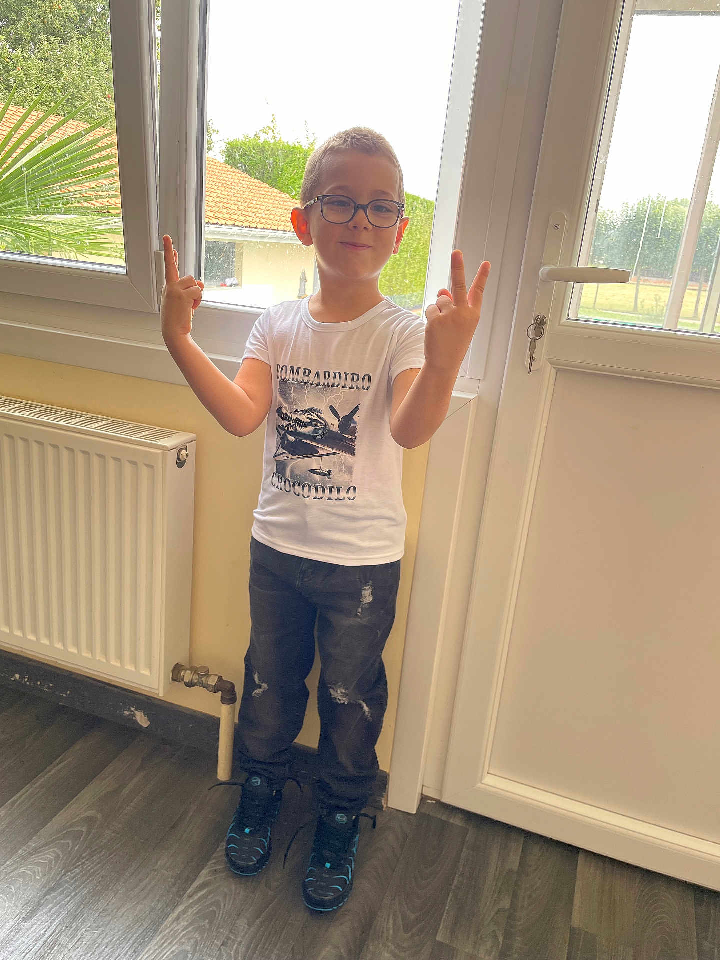 Timëo a rejoint le concours — aidez-le/la à gagner de superbes lots ! child, boy, glasses, full_body, standing, indoor, window, door, radiator, tshirt, jeans, sneakers, pose, peace_sign, smile, flooring, plant, home_interior, portrait, casual_clothing