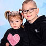 child, children, siblings, portrait, studio_background, blue_background, glasses, pigtails, heart_shirt, pink_pants, hoodie, smile, serious_expression, sitting, indoor, cute, family, face, haircut, young_child