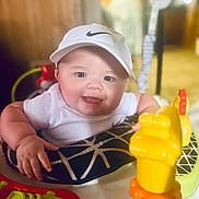 Dawson is registered to the contest to win money with this photo: baby, bright_colors, cheerful, child, chubby_cheeks, clothing, cute, face, happy, headwear, indoor, infant, person, plastic_toy, play_seat, seat, smiling, toy, white_cap, young_child
