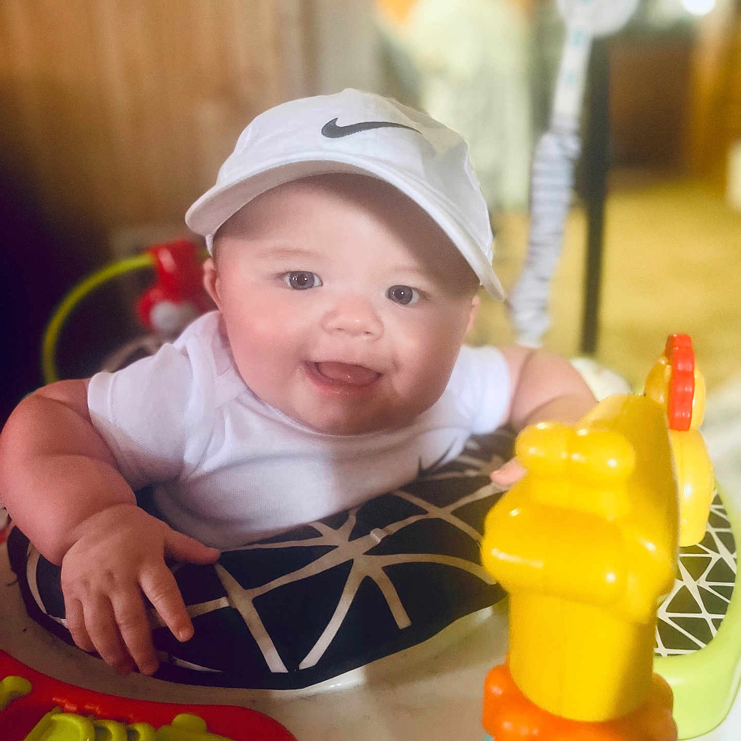 Dawson is registered to the contest to win money with this photo: baby, bright_colors, cheerful, child, chubby_cheeks, clothing, cute, face, happy, headwear, indoor, infant, person, plastic_toy, play_seat, seat, smiling, toy, white_cap, young_child