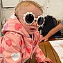 adult, arm, baby, casual, child, clothing, cool, curious, face, fashion, hand, head, heart_pattern, indoor, person, pink_jacket, sunglasses, table, toddler, wood