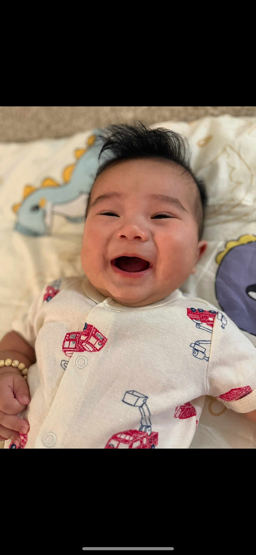 Myles joined the competition — help win amazing prizes! baby, smiling, infant, onesie, fire_truck, blanket, dinosaur, happy, cute, portrait, child, lying_down, indoors, baby_clothes, cheerful, young_child, human, face, baby_bracelet, playful