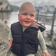 Jacob joined the competition — help win amazing prizes! toddler, child, smile, outdoor, waterfront, rock, vest, puffer_jacket, happy, person, baby, face, blue_eyes, hand, clothing, nature, blurred_background, cold_weather, casual, cute