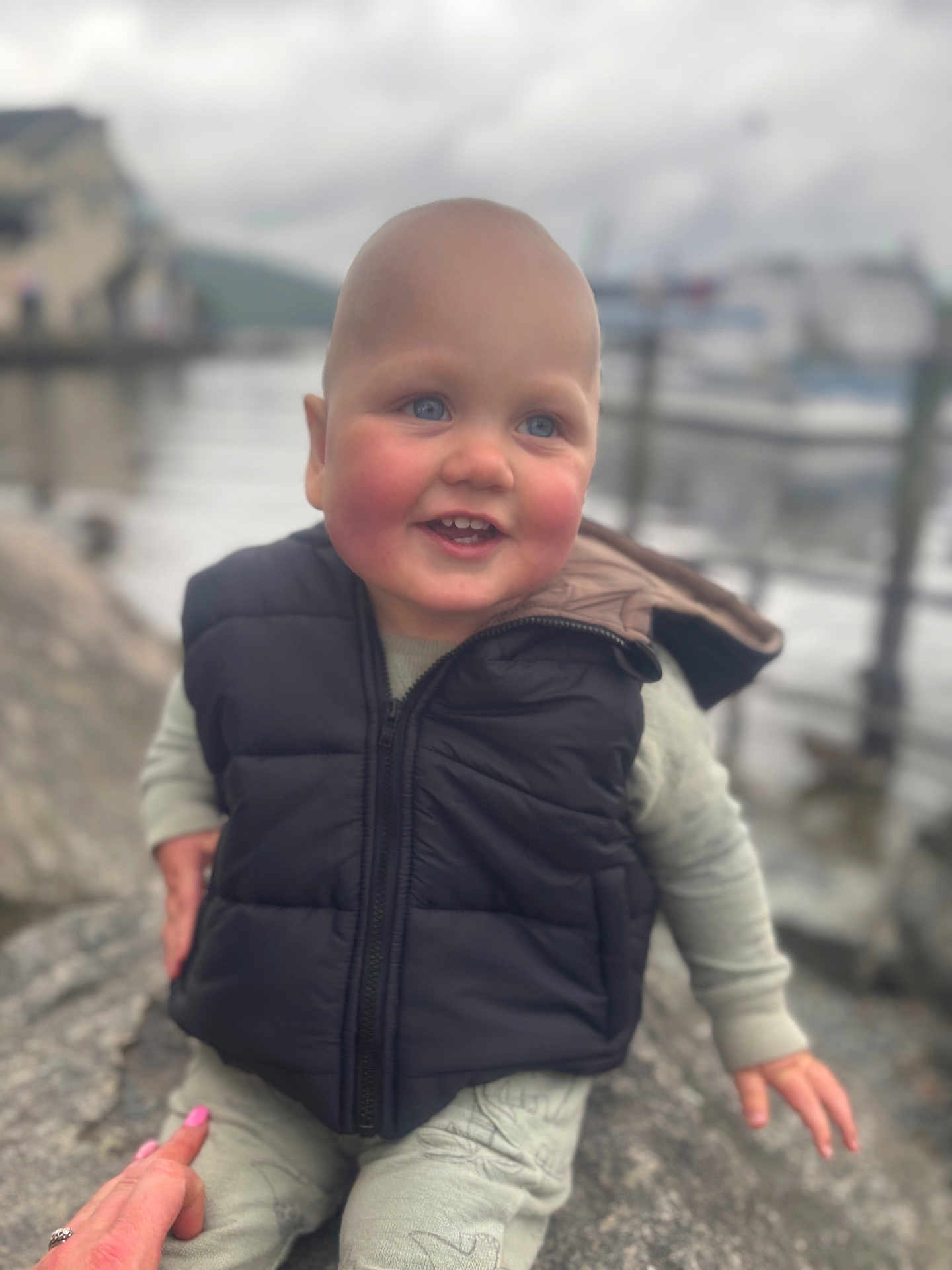 Jacob joined the competition — help win amazing prizes! toddler, child, smile, outdoor, waterfront, rock, vest, puffer_jacket, happy, person, baby, face, blue_eyes, hand, clothing, nature, blurred_background, cold_weather, casual, cute