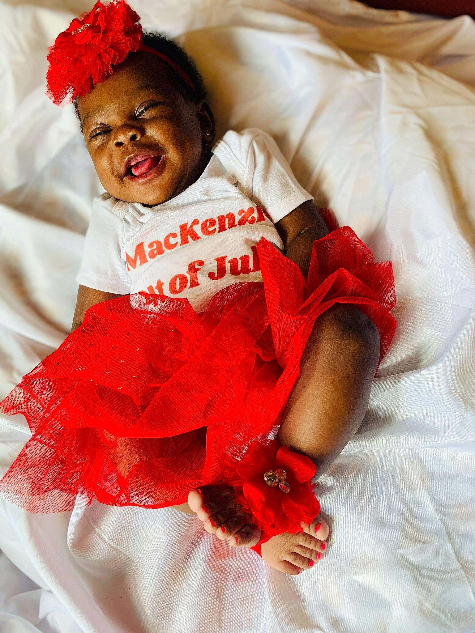 Mackenzie is registered to the contest to win money with this photo: baby_toddler_clothing, child, comfort, day_dress, dress, face, finger, gesture, happy, headwear, linens, magenta, orange, person, petal, pink, red, ruffle, skin, sleeve